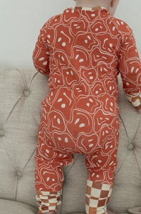 a baby is sitting on a couch in a red and white patterned jumpsuit